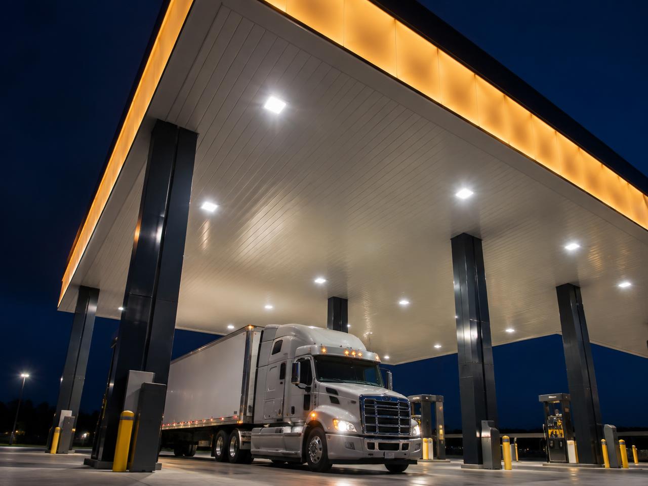 Looking up at a tall, brightly lit canopy at night with a semi-truck beneath